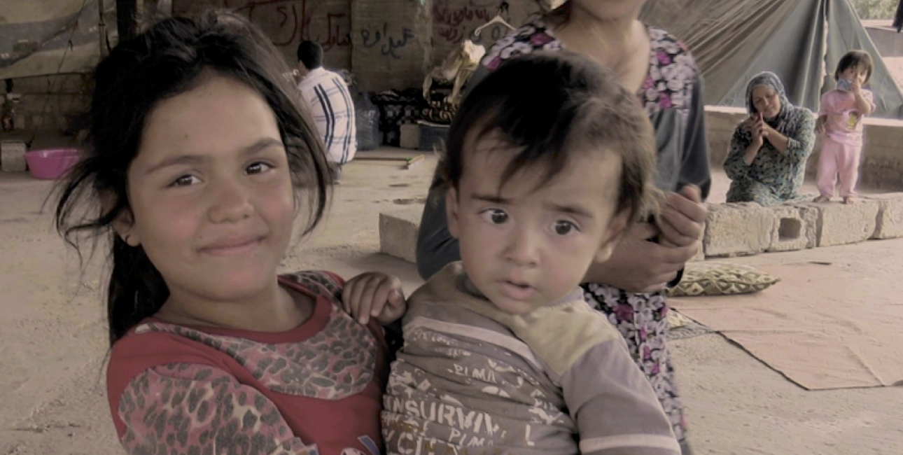 Pigen her er flygtet fra Irak sammen med sin familie. I en måned har hun sammen med sin søster sovet på den kolde jord, men nu smiler hun, fordi hun har fået en madras af Bibelselskabet. Foto: Andrea Rhodes, De Forenede Bibelselskaber