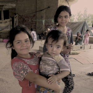 Pigen her er flygtet fra Irak sammen med sin familie. I en måned har hun sammen med sin søster sovet på den kolde jord, men nu smiler hun, fordi hun har fået en madras af Bibelselskabet. Foto: Andrea Rhodes, De Forenede Bibelselskaber